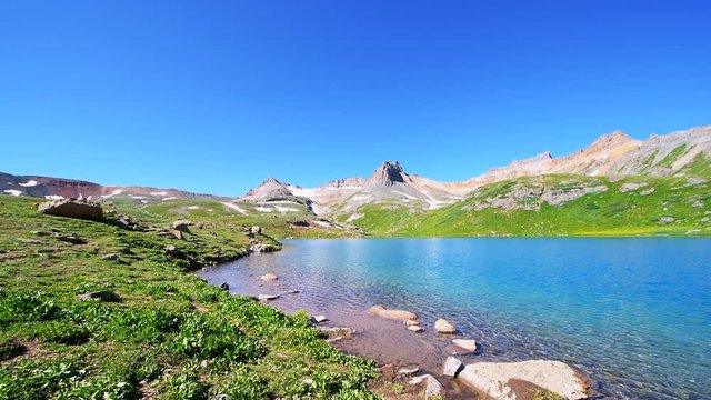 Panning panorama view on cold colorful turquoise water of Ice Lake on hiking trail in Silverton, Colorado in San Juan Mountains summit peak with snow