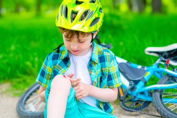 A boy who fell from a Bicycle on a walk in the Park looks at the broken knee with regret.Abrasions and wounds of children during summer walks