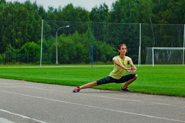 Fototapeta premium A woman does sports exercises in the open air. A brunette in a yellow sports shirt and shorts trains at the stadium.