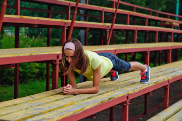 Young slender attractive brunette in doing exercises on a bench in an outdoor stadium, basic training and fitness concept.