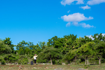 青空と森の背景にいるスーツケースを持った女性