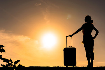 太陽を背景にスーツケースを持った女性のシルエット