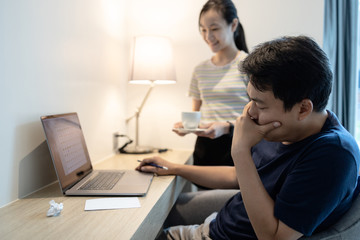 Asian man with a laptop computer working at home,feeling stress tired,close eyes and thinking of problem solution about difficult,child girl holding a cup of tea or coffee serving care of father