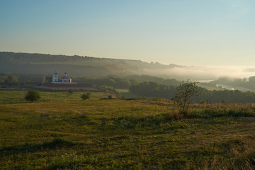 Fototapeta premium Summer time. Morning dawn over the river in a hazy, thoughtful haze. Beautiful view of the forest and river covered with fog early in the morning.