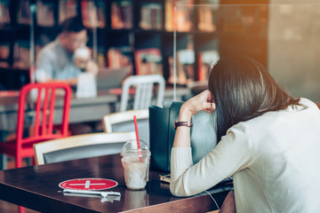 Back view of Asian woman use smartphone and relax with beverage in coffee shop, where seats are spaced for social distancing during the Corona virus (COVID-19) epidemic. New normal lifestyle