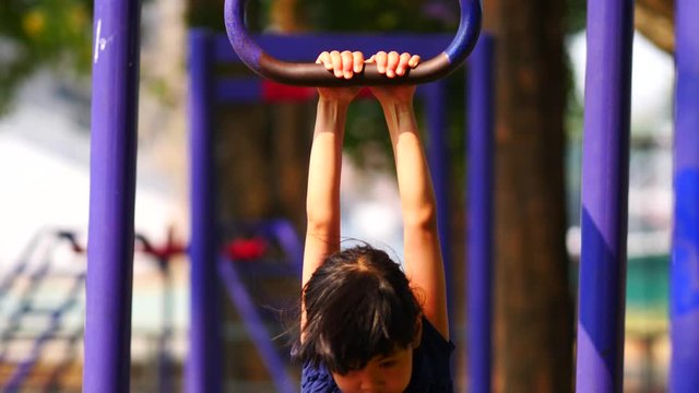 Asian girl hanging on monkey bars at playground