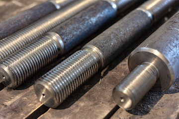 After turning and milling, the threaded studs lie on a wooden rack in the warehouse.