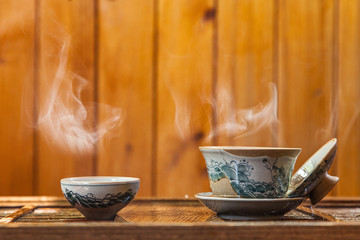 Dishes for traditional chinese tea ceremony with splashing hot water and a cloud of steam on a wooden background