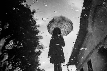 Silhouette of young girll with lace parasol reflected in puddle