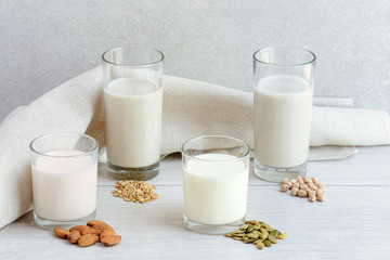 Four different glasses of vegan non dairy milk from nuts, seeds, cereals and legumes
