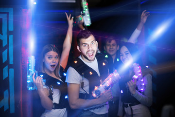 Group portrait of young people in colorful beams of laser guns having fun on lasertag arena