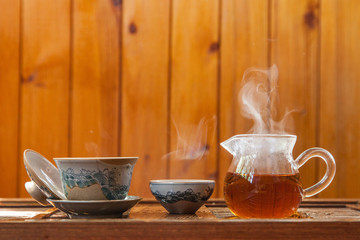 Dishes for traditional chinese tea ceremony with splashing hot water and a cloud of steam on a wooden background