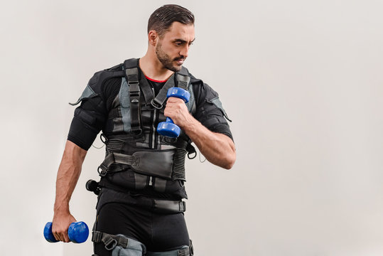 Sporty man in electrical muscular stimulation suit doing exercise with dumbbells