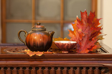 Chinese kettle and tea cups on vintage wooden table with autumn leaves and cloud of vapor