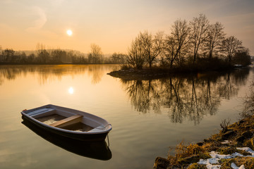 Broken rowboat anchored on riverbank on cold winter morning