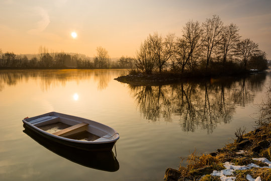 Broken rowboat anchored on riverbank on cold winter morning - Powered by Adobe