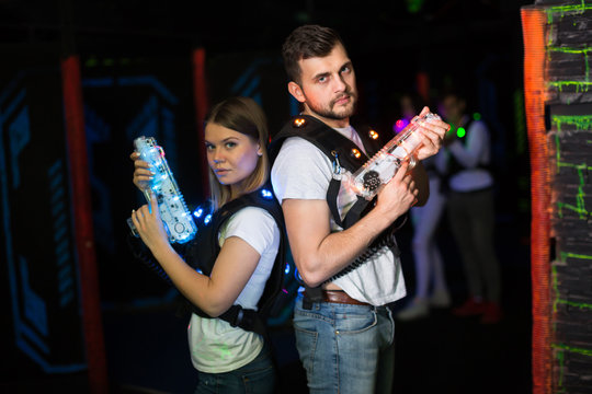 Young man and woman standing back to back with laser pistols in dark lasertag room