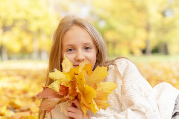 beautiful blonde teen girl sitting on the grass in an autumn Park with maple trees