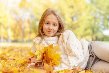 Naklejka na ściany i meble beautiful blonde teen girl sitting on the grass in an autumn Park with maple trees