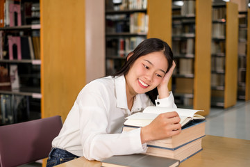 Young Asian women are searching for books and reading from the bookshelves in the college library to research and develop themselves in education