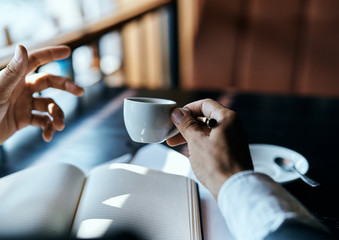 A man holds in his hand a cup of coffee pen books documents cafe