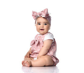 Surprised infant baby toddler in polka dot dress and headband with bow sits on the floor looking at camera
