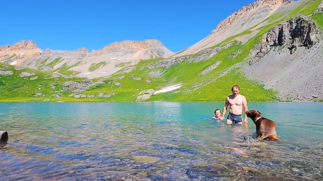 Slow motion of young couple, man and woman in bikini swimsuit and rhodesian ridgeback brown dog shaking off water, swimming in cold Ice Lake water, Silverton Colorado at San Juan Mountains summit peak