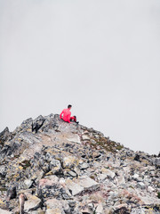 A lone traveler sits on the edge of a mountain cliff in the fog and looks into the abyss