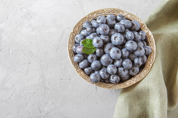 Fresh blueberries in bowl. Fresh blueberries with green leaves on gray table. Concept for healthy eating and nutrition. Top view. Copy space.