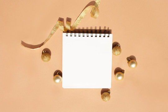 Blank notebook for notes and Christmas tree golden toys on a beige background. To do list