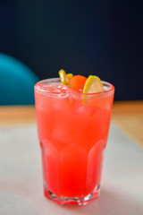 Citrus fruit cocktail in nice red color in front of a black background. Served in a wine glass on a wooden table.