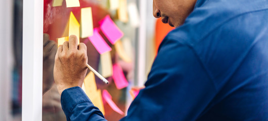 Casual creative businessman planning strategy analysis putting post it stickers note to share idea for startup project on glass board at modern office