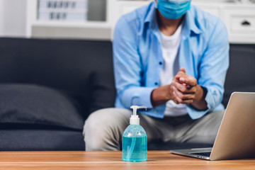 Young man washing hands with alcohol gel in quarantine for coronavirus wearing protective mask with social distancing and using laptop computer working at home.work from home and covid19 concept