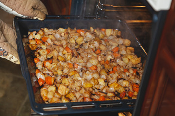 Hands in mittens take out baking tray with vegetables oven