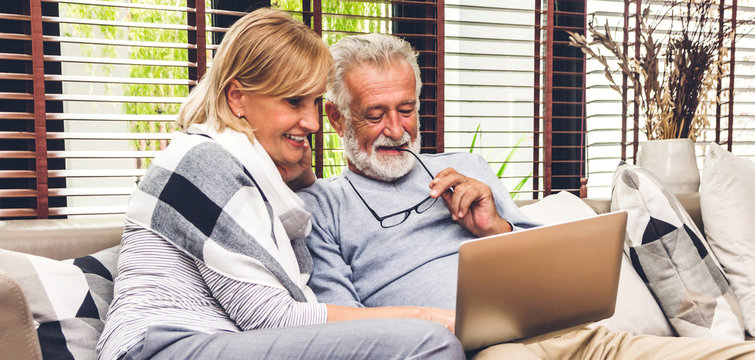 Senior couple family having good time using laptop computer together.Happy elderly husband and wife checking social media and reading news or shopping online while sitting on sofa at home.Retirement 