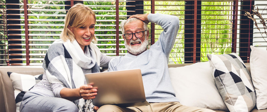 Senior couple family having good time using laptop computer together.Happy elderly husband and wife checking social media and reading news or shopping online while sitting on sofa at home.Retirement