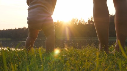 Parents and baby standing barefoot on grass at sunset by the lake. Single parent concept. 