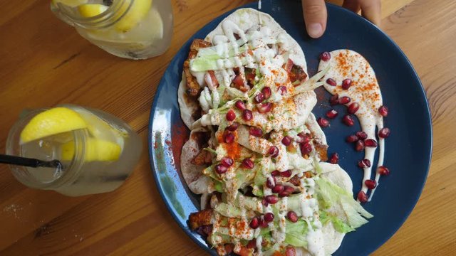 Top view of hand placing dark blue plate with tacos on wooden table. Two jars of lemonade. Clean eating concept