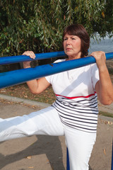 sports pensioner on river bank is engaged in physical exercises