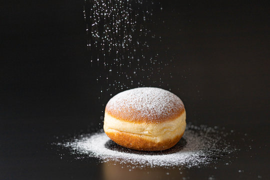doughnut with powdered sugar infront of a black background