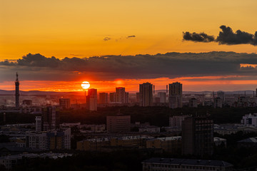 Black silhouettes of buildings are on a red sky background with orange and yellow sunset