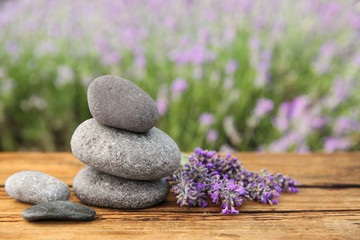 Fototapeta na wymiar Spa stones and fresh lavender flowers on wooden table outdoors, closeup. Space for text