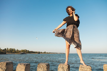 Atmospheric portrait of a young woman in  stylish clothers walking on rock, in the background sea....