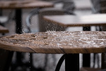 Stoliki w ogródkach restauracyjnych zmoczone letnim deszczem, krople wody rozbijają się na powierzchni stołu.