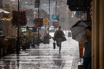 Ulica w deszczu i zmoknięty człowiek biegnący chodnikiem.