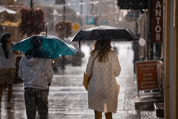 Ulica w deszczu i ludzie z parasolami idący spokojnie chodnikiem.
