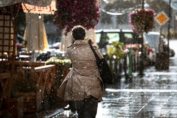 Fototapeta na wymiar Ulica w deszczu i zmoknięty człowiek idący spokojnie chodnikiem.