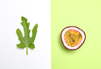 Half of fresh ripe passion fruit (maracuya) and green leaf on color background, flat lay