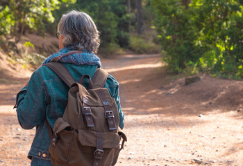 Rear view of a senior woman hiking in the forest with a backpack - active elderly retired enjoying holidays in the nature