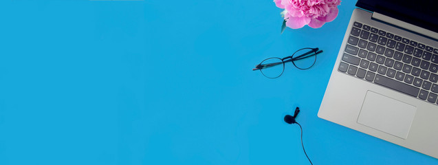 Workspace of a writing desk with a copy space.Computer, microphone, glasses for work on a blue...